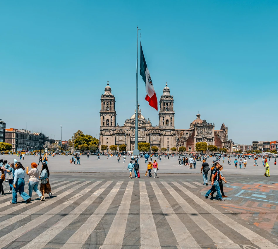 Plaza con bandera de M&eacute;xico y visitantes frente a la catedral de estilo barroco