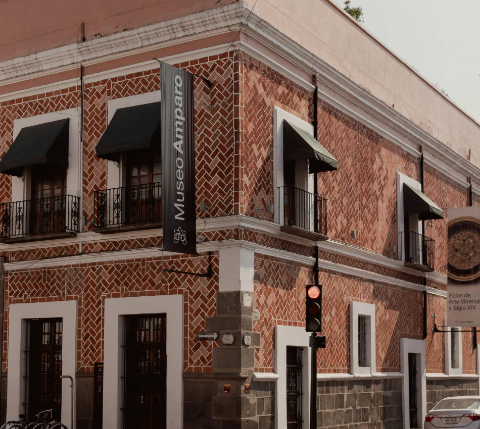Fachada de ladrillo con banderas de &ldquo;Museo Amparo&rdquo; y ventanas con toldos negros