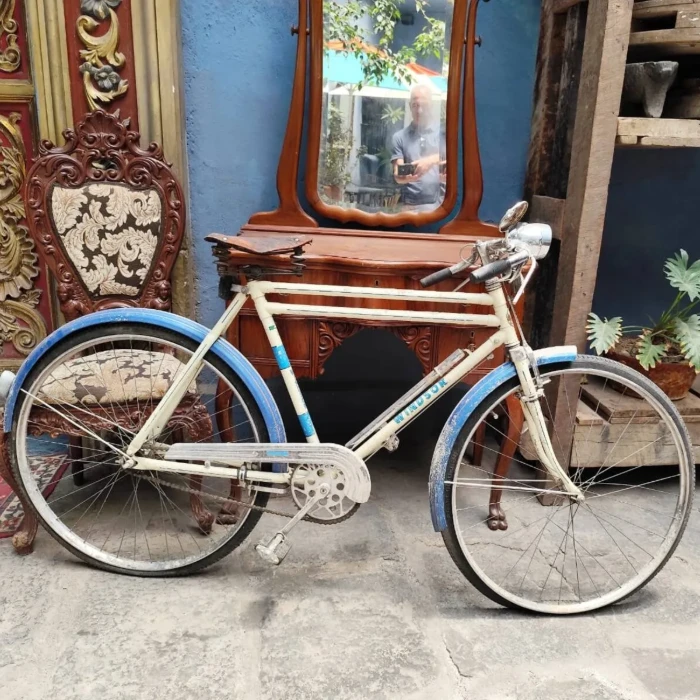 Bicicleta blanca y azul en patio con muebles de madera y pared azul