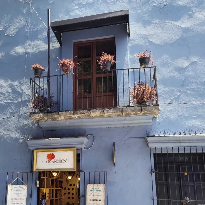 Balc&oacute;n de fachada azul con plantas colgantes y letrero &ldquo;Los &Aacute;ngeles&rdquo;
