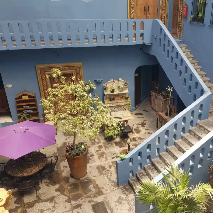Patio interior con escalera azul, plantas y sombrilla morada.