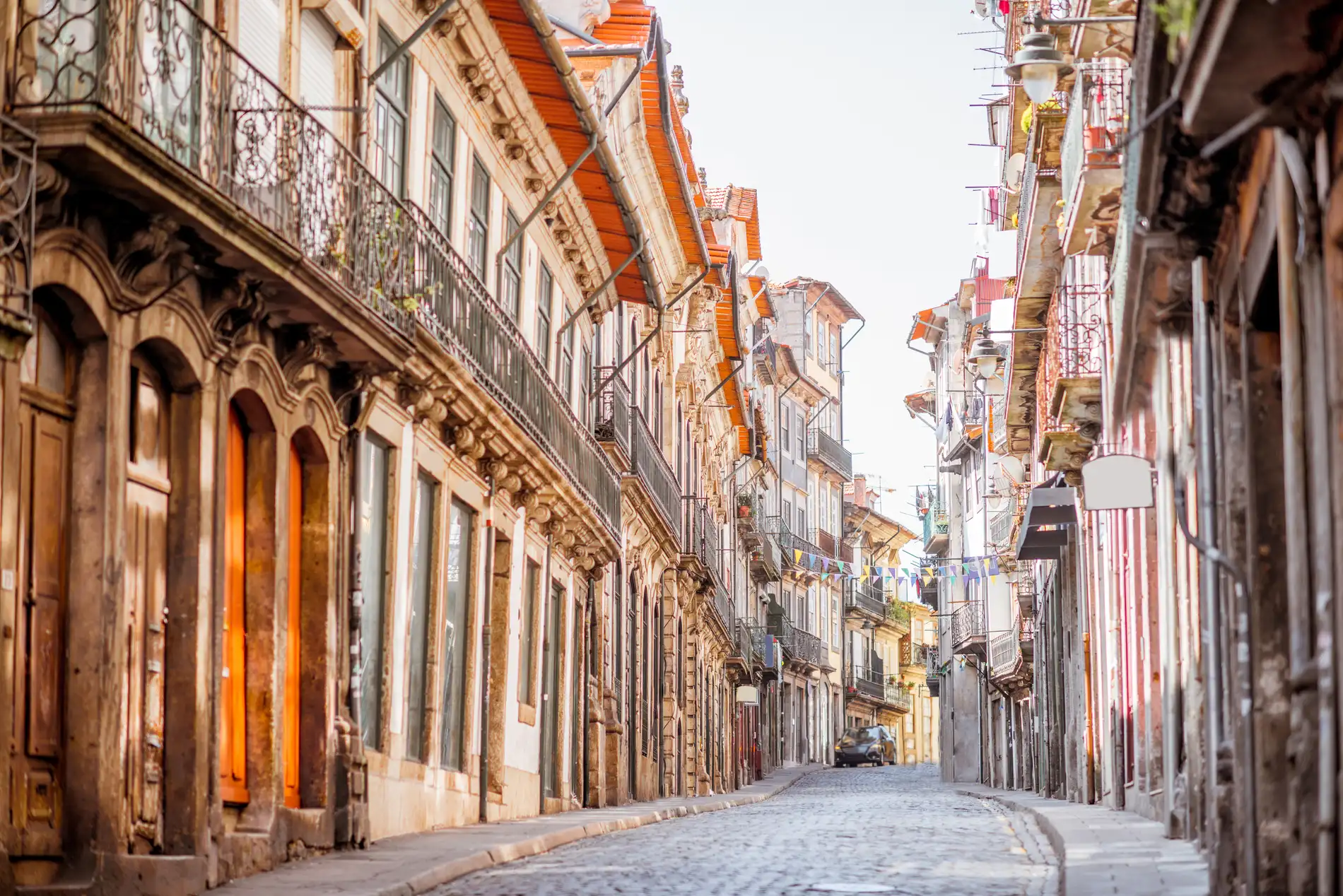 Rua estreita com pr&eacute;dios hist&oacute;ricos e varandas, com luz dourada ao fundo