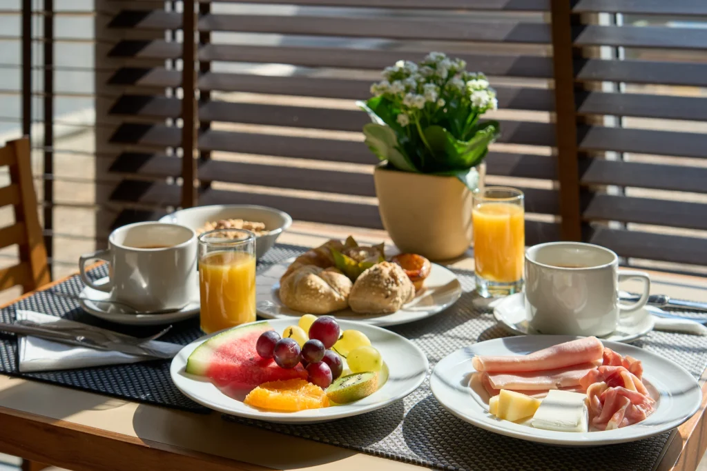 Caf&eacute; da manh&atilde; ao ar livre com frutas, sucos e presunto em mesa de varanda