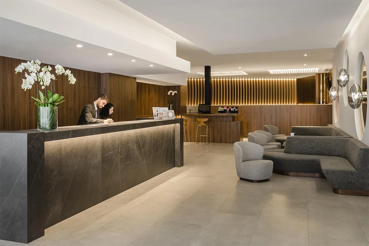 Recep&ccedil;&atilde;o de hotel moderna com poltronas cinzas, balc&atilde;o e decora&ccedil;&atilde;o com flores