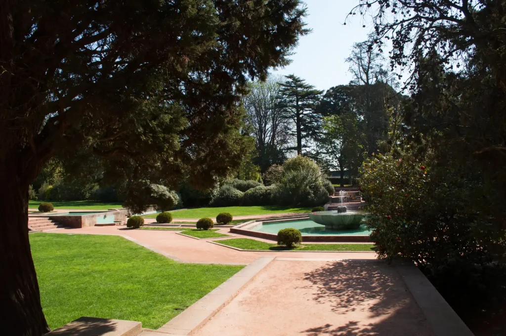 Jardim com gramado, caminhos de pedra e piscina ao fundo, entre &aacute;rvores