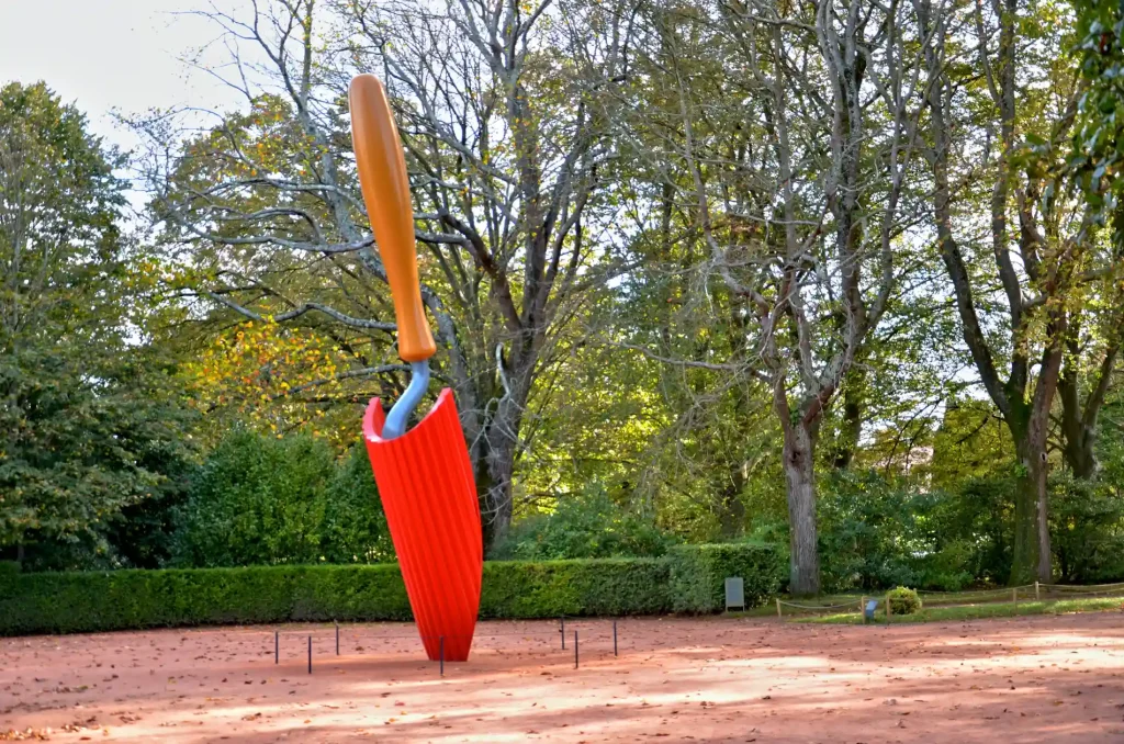 Bandeira vermelha e laranja em vara no parque, com &aacute;rvores ao fundo