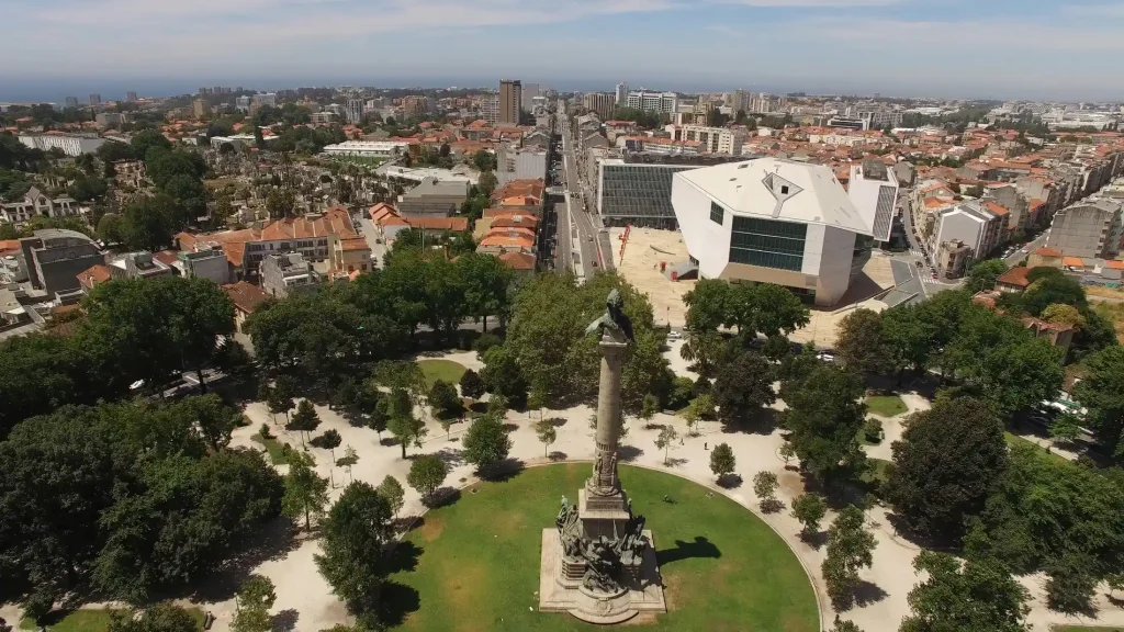 Vista a&eacute;rea de pr&eacute;dio branco e jardim com monumento no centro urbano