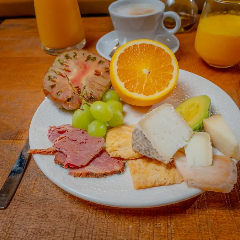 Desayuno con jam&oacute;n, queso, frutas y rodaja de naranja en plato blanco