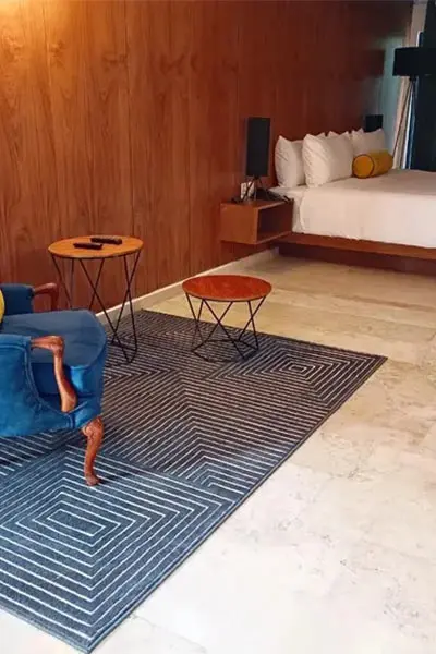 Sala de hotel con cama, alfombra azul y mesas auxiliares circulares