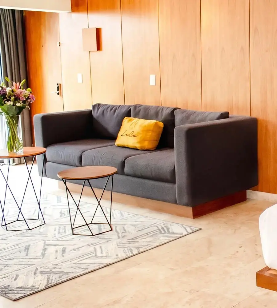 Sala moderna con sof&aacute; gris, coj&iacute;n amarillo y mesitas de madera y metal