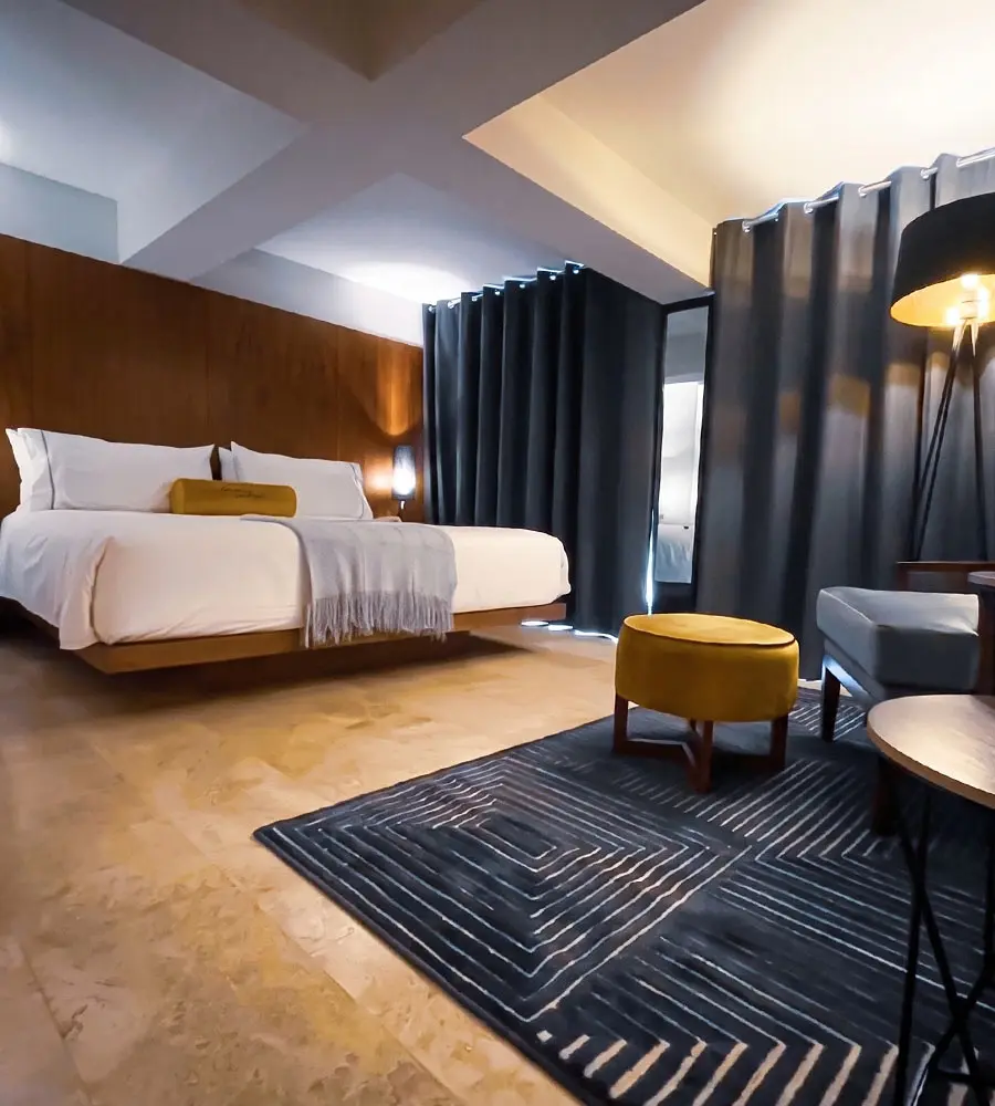Habitaci&oacute;n de hotel moderna con cama, alfombra oscura y sill&oacute;n amarillo