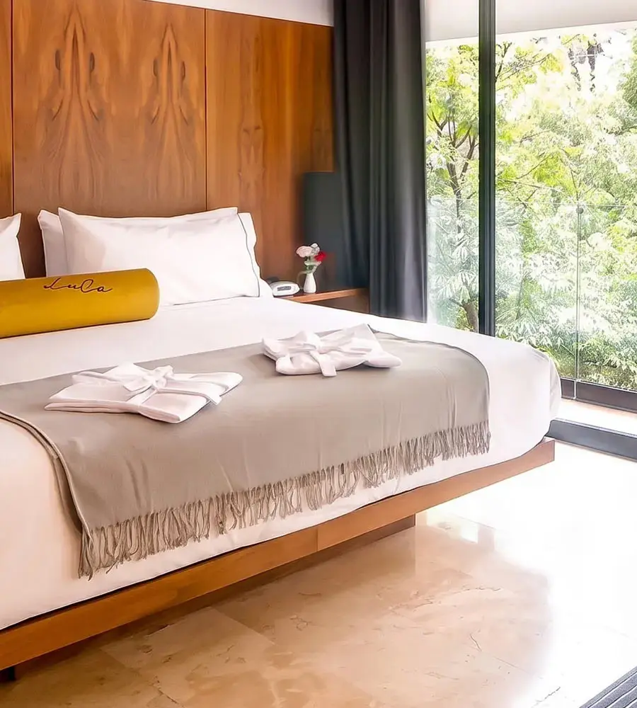Habitaci&oacute;n moderna con cama blanca y ventana con vista al jard&iacute;n verde