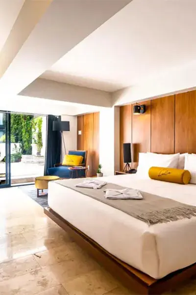 Habitaci&oacute;n de hotel moderna con cama, sill&oacute;n y balc&oacute;n con cortinas