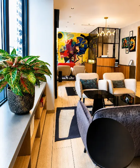 Salon moderne avec fauteuils, tapis, &oelig;uvres murales et plante en pot pr&egrave;s d&rsquo;une fen&ecirc;tre