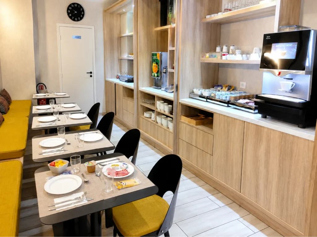 Salle de petit-d&eacute;jeuner avec buffet en bois, horloge et tables dress&eacute;es