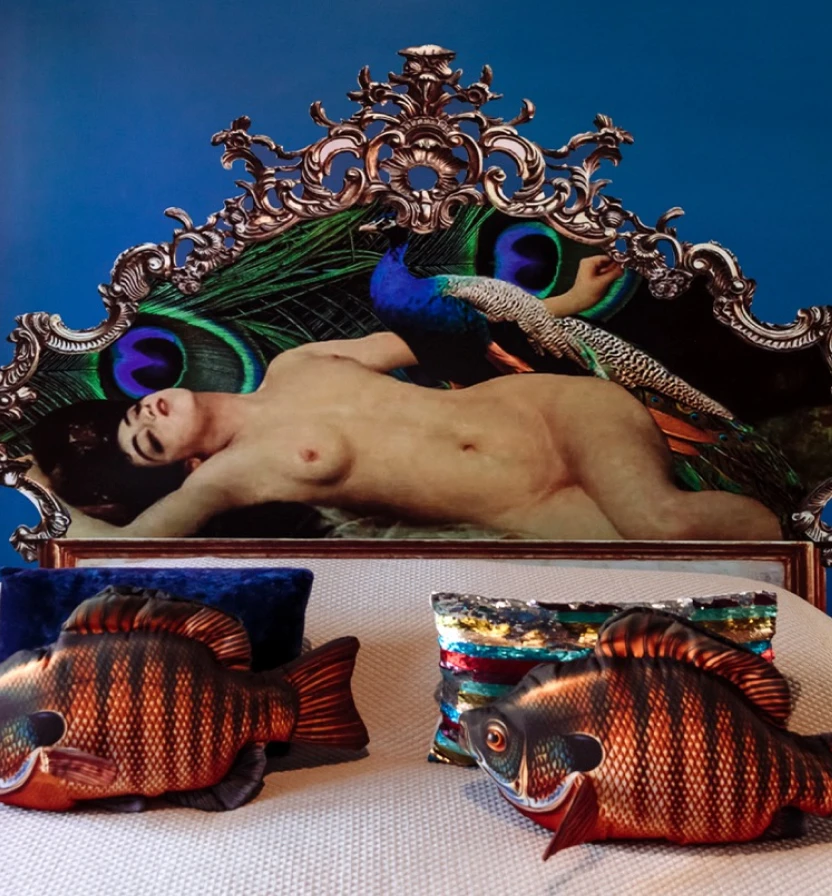 Surreal nude man on ornate peacock-feather couch with colorful fish pillows