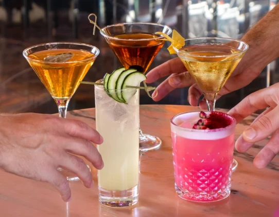 People clinking martini and pink cocktails with citrus garnish in glasses