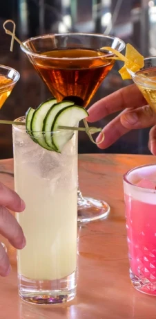 Bartender garnishing a layered cocktail with cucumber slices, drinks nearby