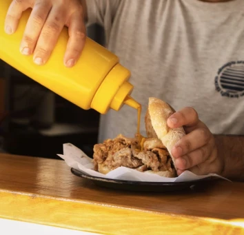 Hand pouring filling into pita pocket on a wooden counter from yellow dispenser