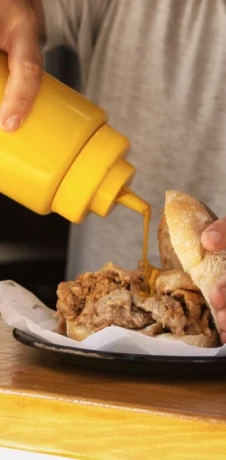 Hand squeezes yellow sauce onto a bread piece with meat filling