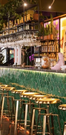 Bar with green patterned counter, stools, and hanging lights and bottles.