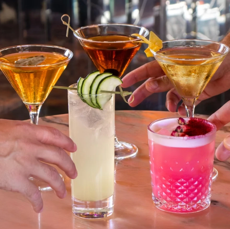 Three cocktails in glasses being clinked, with citrus and berries garnish