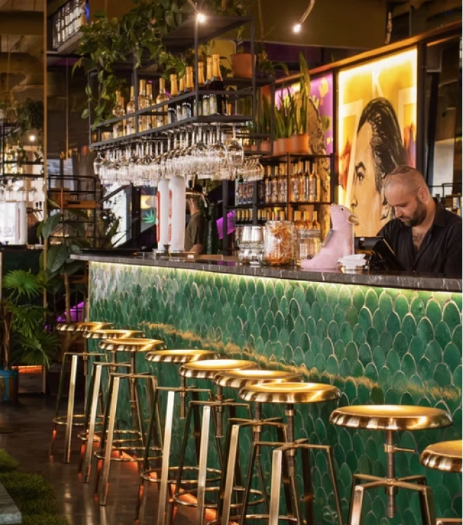 Bartender at bar with sparkling glasses, neon lights, and gold stools at night