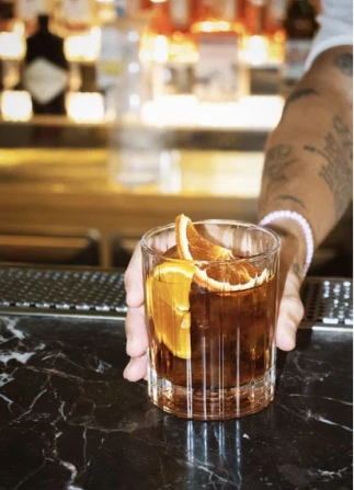 Person holding a mug of amber beer with orange garnish on a bar counter