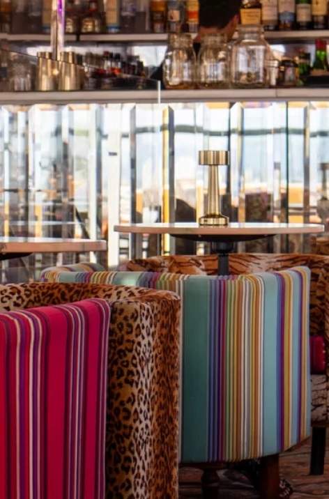 Colorful striped and patterned chairs in a bar with bottles behind them