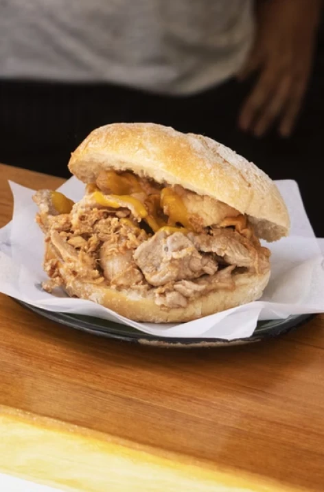Pulled pork sandwich with melted cheese on a wooden table.