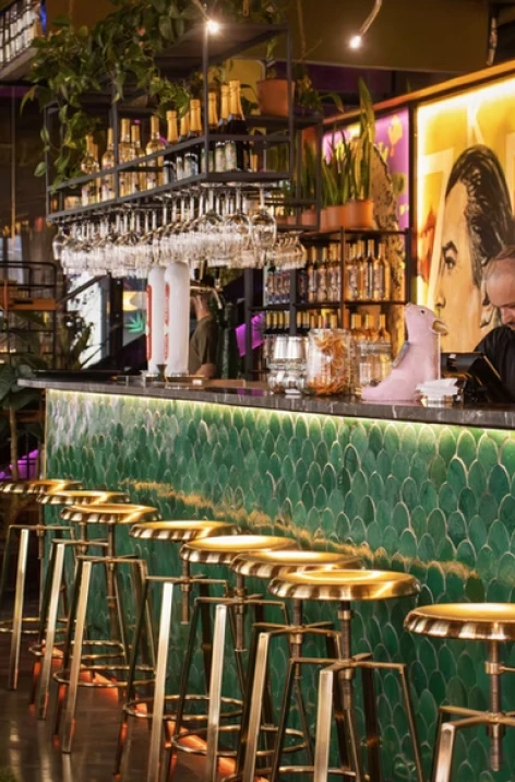 Bar with gold stools, glassware, and bottles under warm lights in a lounge.