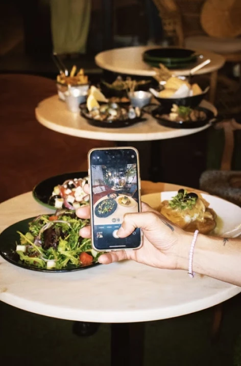 Hand holds phone over plated food spread on a round table in restaurant