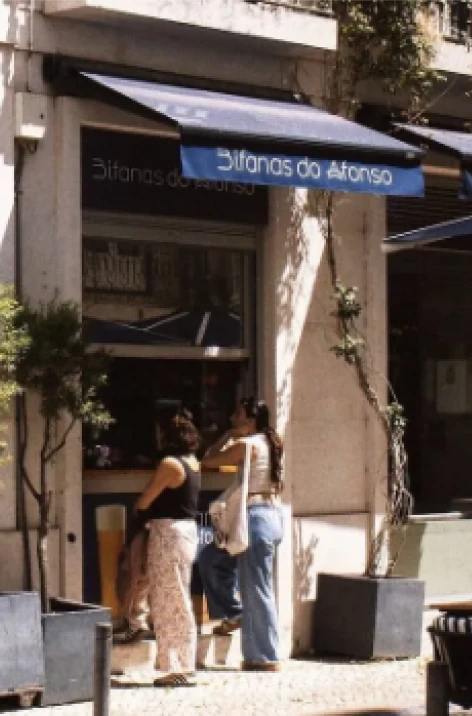 People walking near a kiosk with a blue sign reading &ldquo;S&iacute;tios do Alfonso&rdquo;