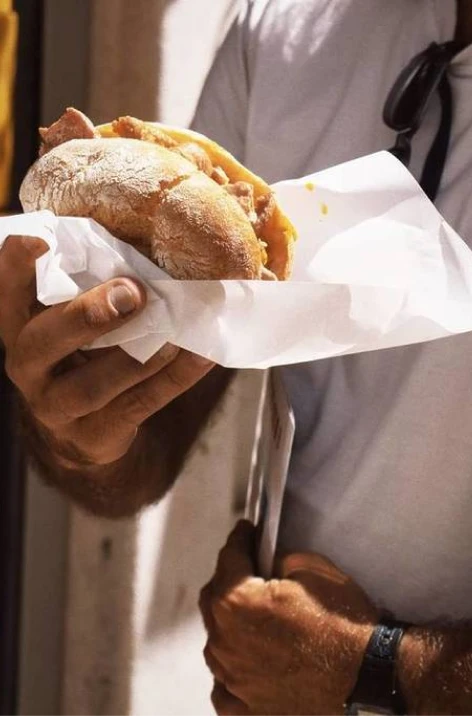 Hands holding a warm baguette wrapped in paper, with lemon butter.