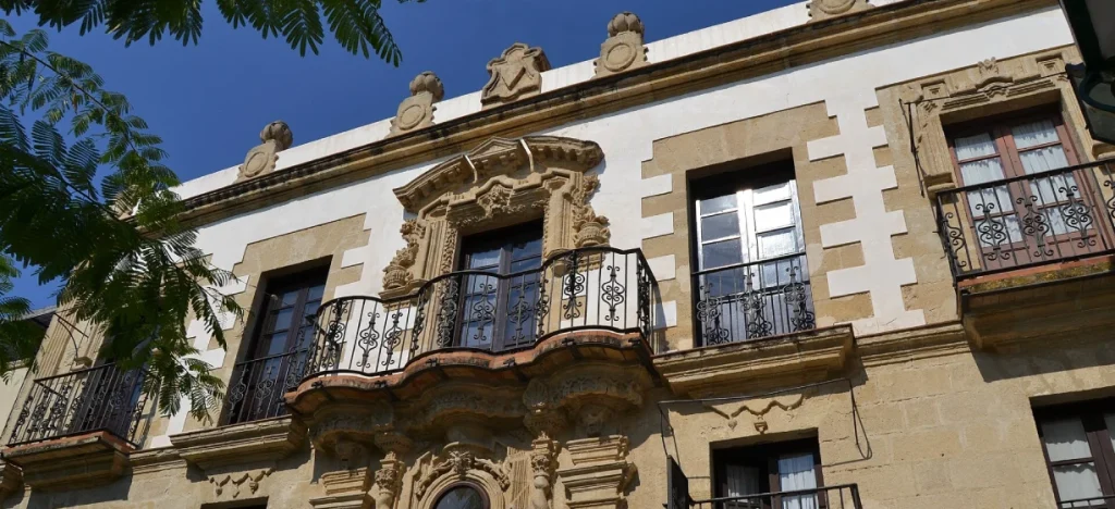 Fachada hist&oacute;rica con balcones de hierro y ornamentaci&oacute;n, bajo cielo azul