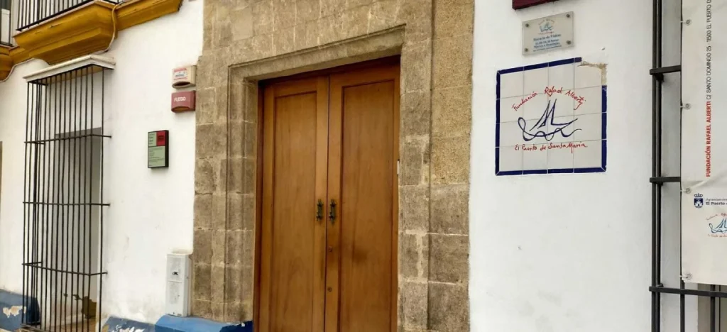 Puerta de madera y pared de piedra con cartel y firma pintada en azul y rojo.