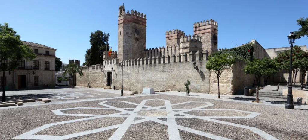 Plaza con mosaico blanco, murallas y torre medieval bajo cielo azul