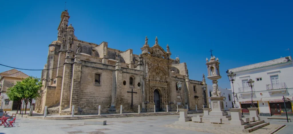 Iglesia de piedra y plaza con farolas y edificios, cielo azul.