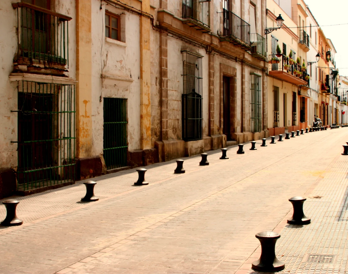Calle estrecha con edificios antiguos y farolas en fila con bolardos negros