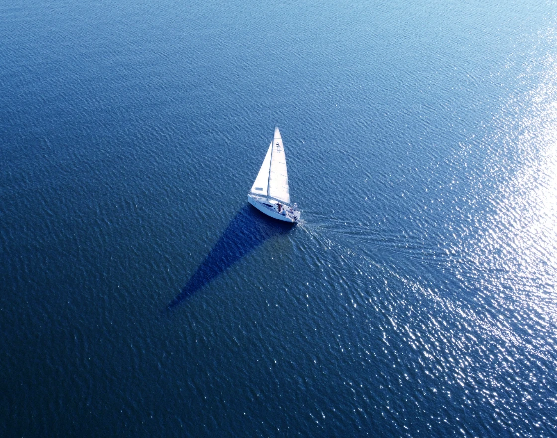 Velero blanco navegando sobre el mar azul con reflejos del sol