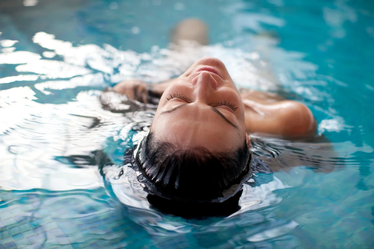 Mujer sonriendo bajo el agua en una piscina, con burbujas y reflejos