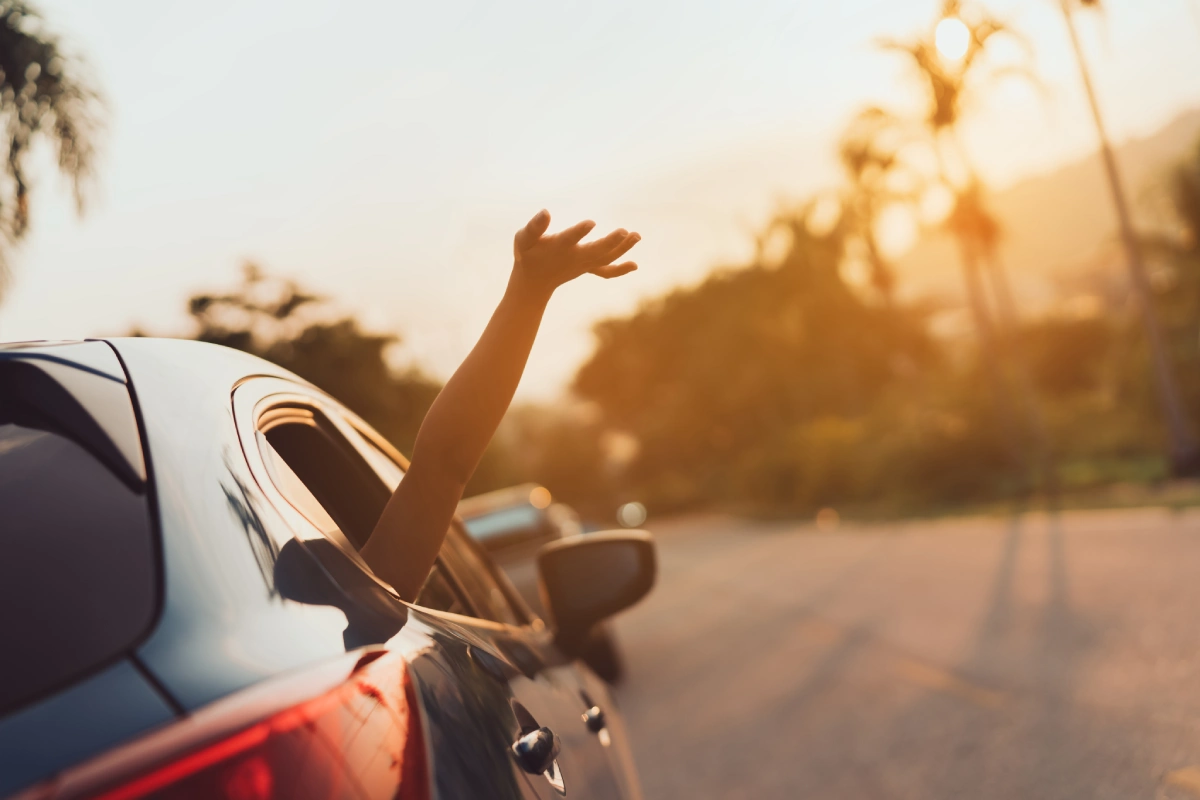 Ni&ntilde;a levanta la mano desde el asiento del coche al atardecer