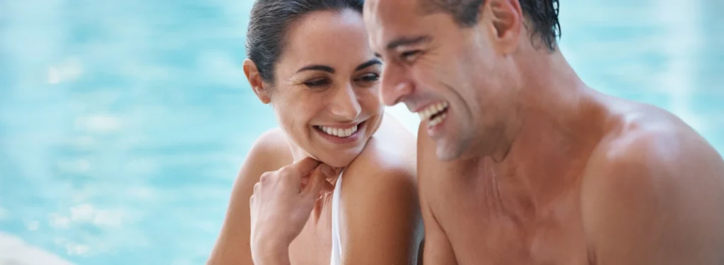 Pareja sonriente junto a la piscina, hombre y mujer relajados al sol