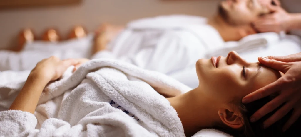 Mujer relaj&aacute;ndose en una camilla, con terapeuta realizando masaje en el rostro