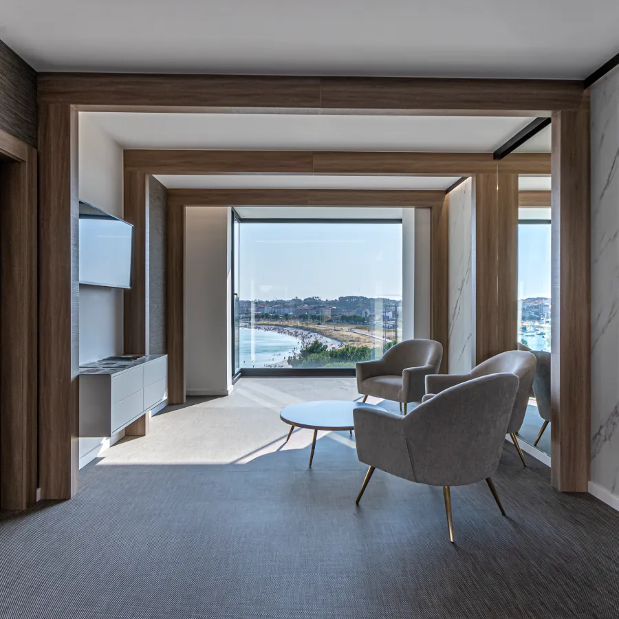 Sala moderna con sillones grises y grandes ventanales hacia el r&iacute;o