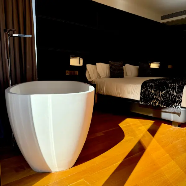 Suite moderna con cama y ba&ntilde;era blanca en habitaci&oacute;n oscura.