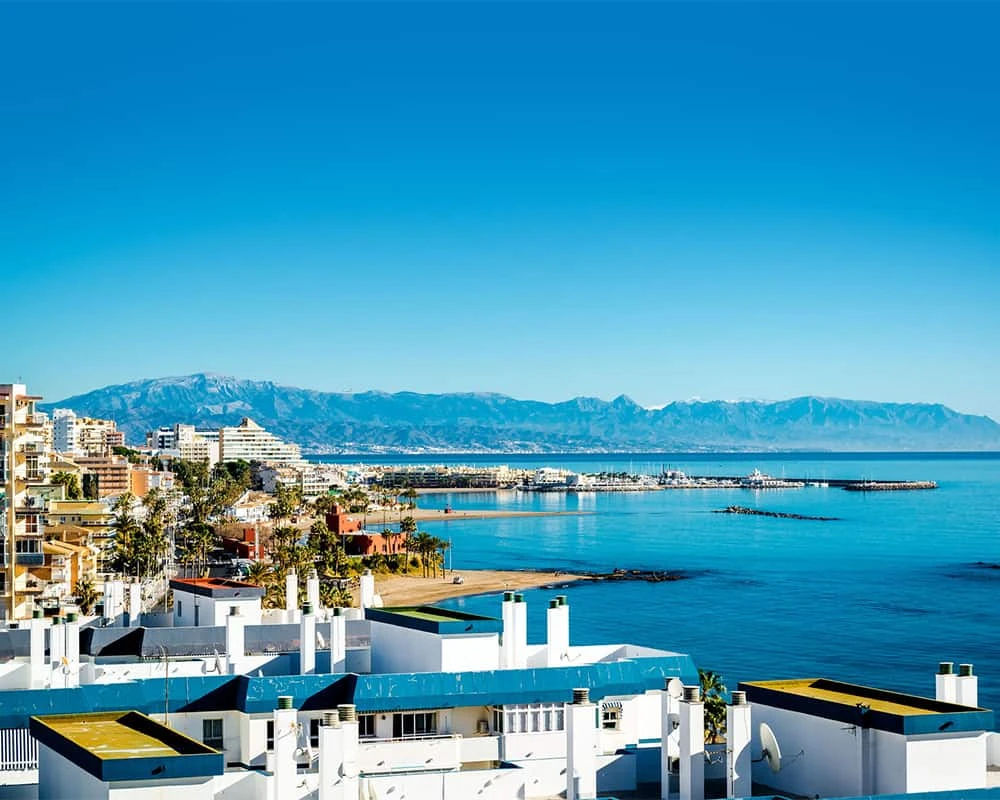 Costa y ciudad blanca junto al mar azul con monta&ntilde;as al fondo