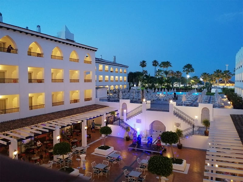 Patio de hotel con mesas para eventos, iluminaci&oacute;n nocturna y palmeras