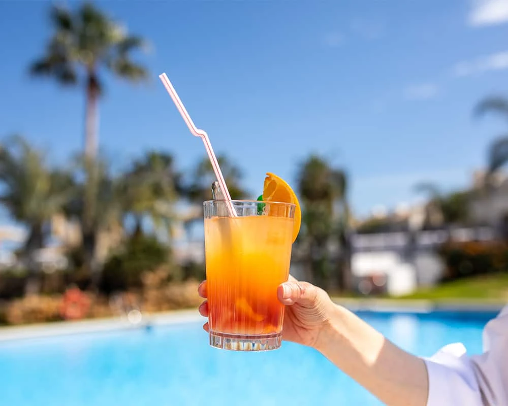 Vaso de c&oacute;ctel naranja con pajita rosa junto a la piscina en verano