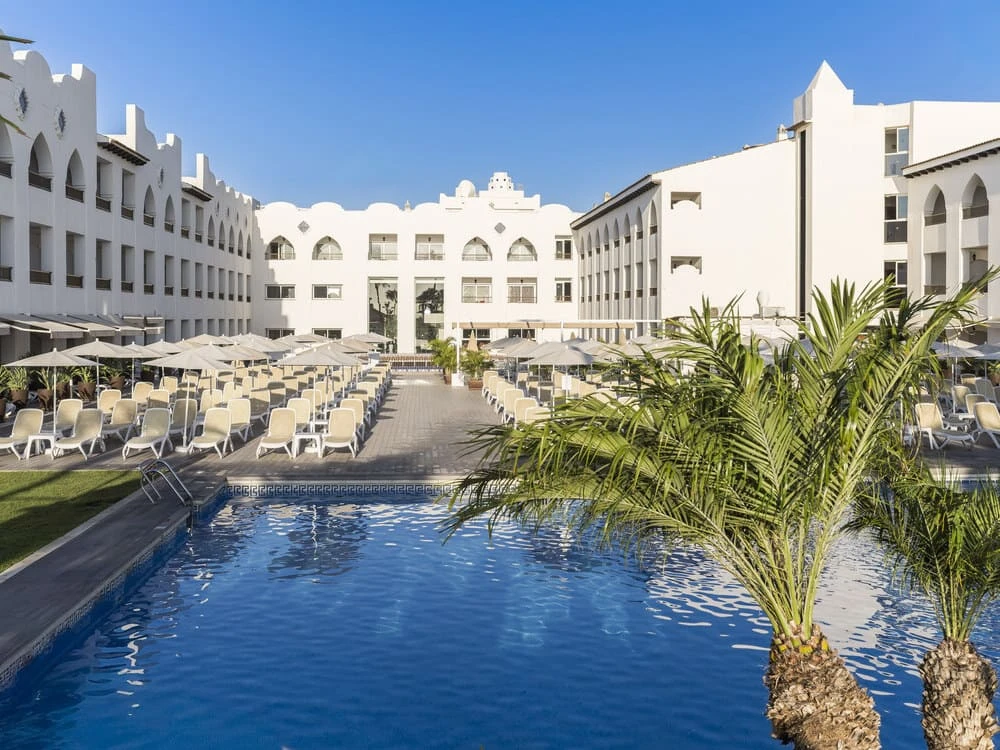 Piscina y patio con tumbonas en complejo hotelero blanco al cielo azul